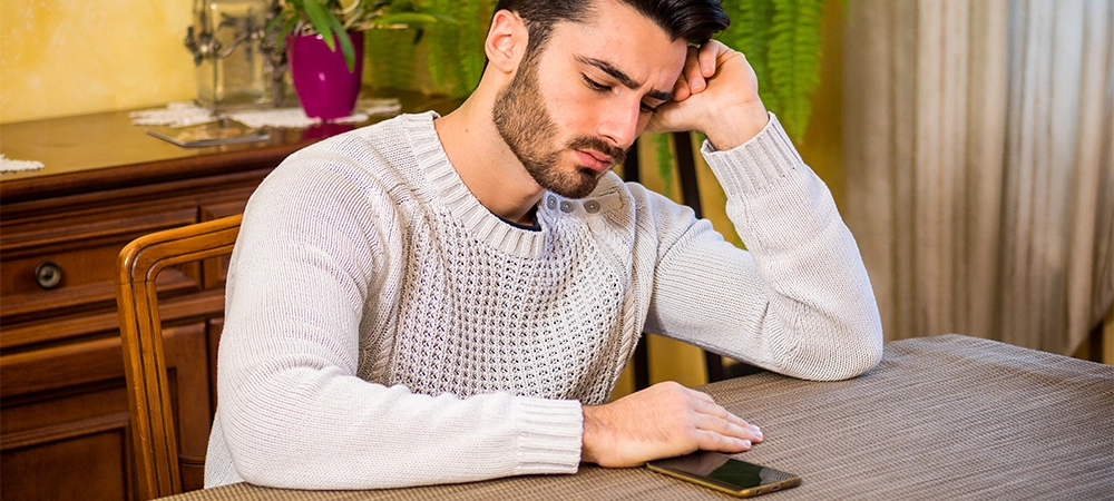 Young man sitting at table and waiting for call or message at home