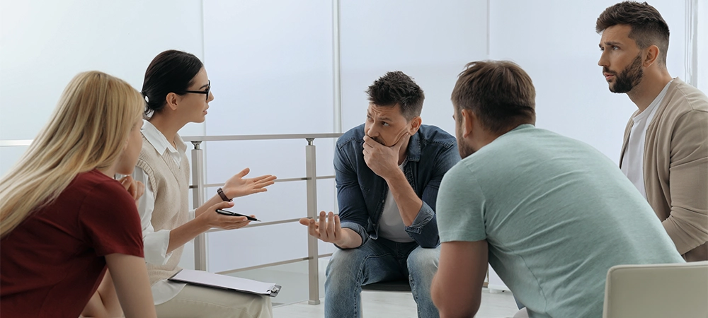 Psychotherapist working with group of drug addicted people at therapy session indoors