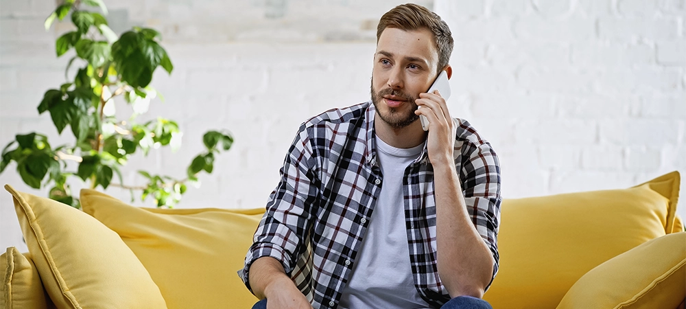 bearded man talking on smartphone while sitting on couch