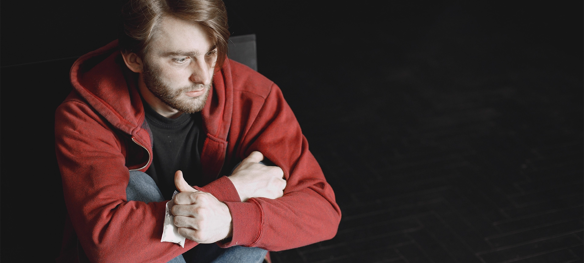 Young addicted man with cocaine packet sitting alone