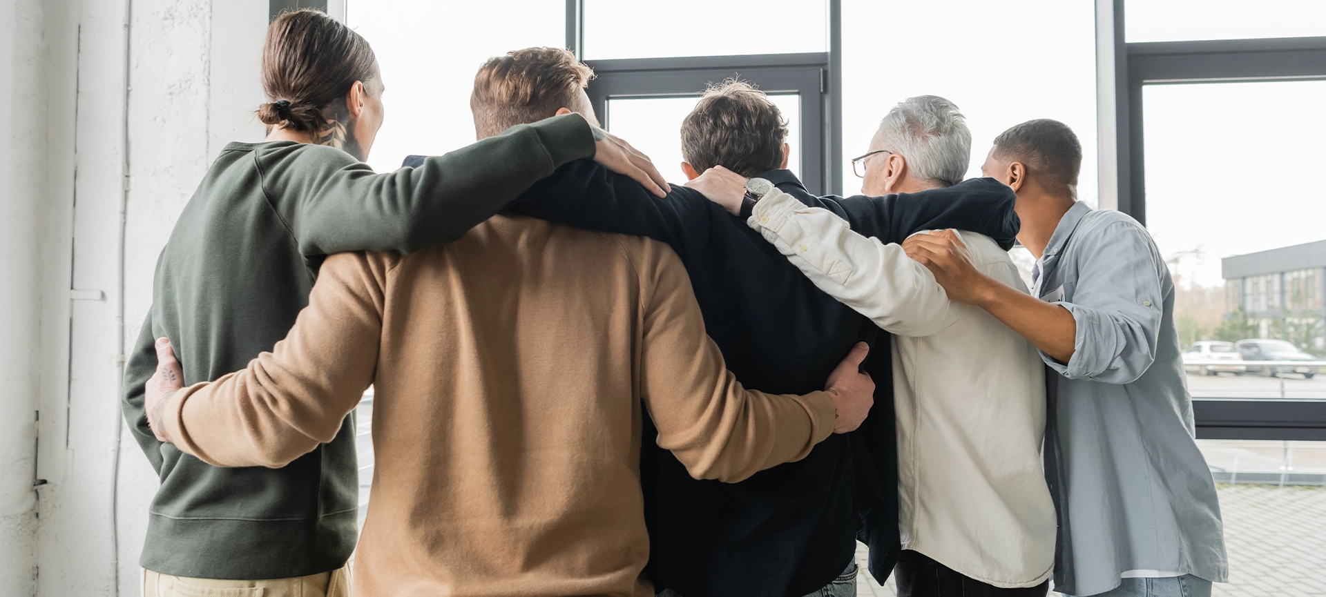 back view of multiethnic people with drug addiction hugging during therapy in rehab center