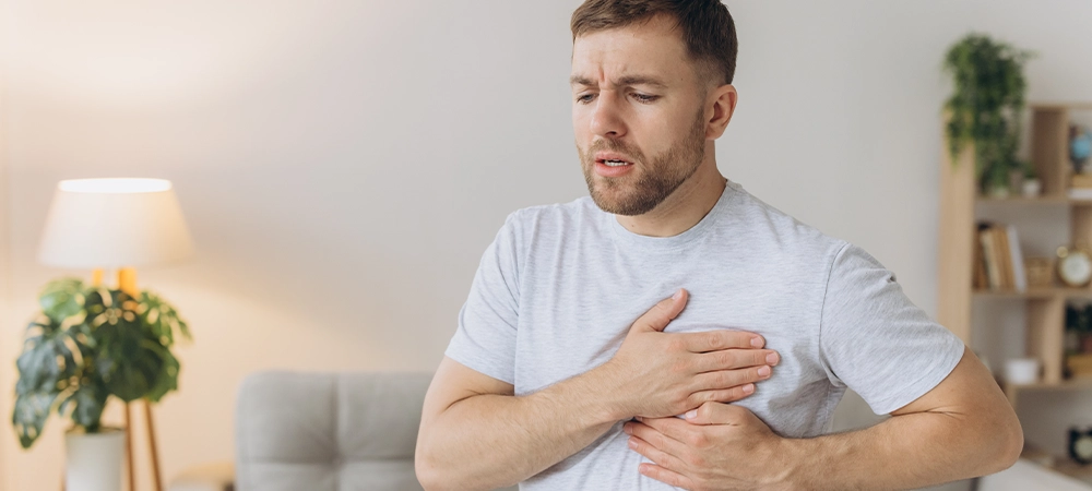 young man is standing at home and holding his chest feels severe pain