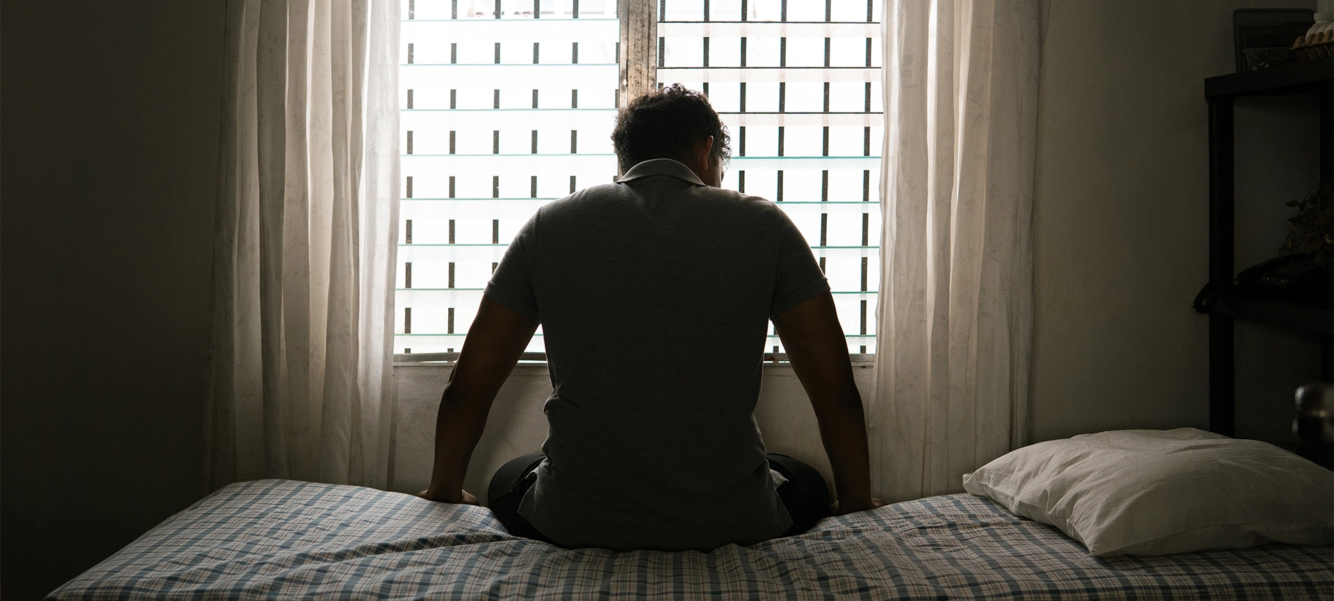 desperate man in silhouette sitting on the bed alone