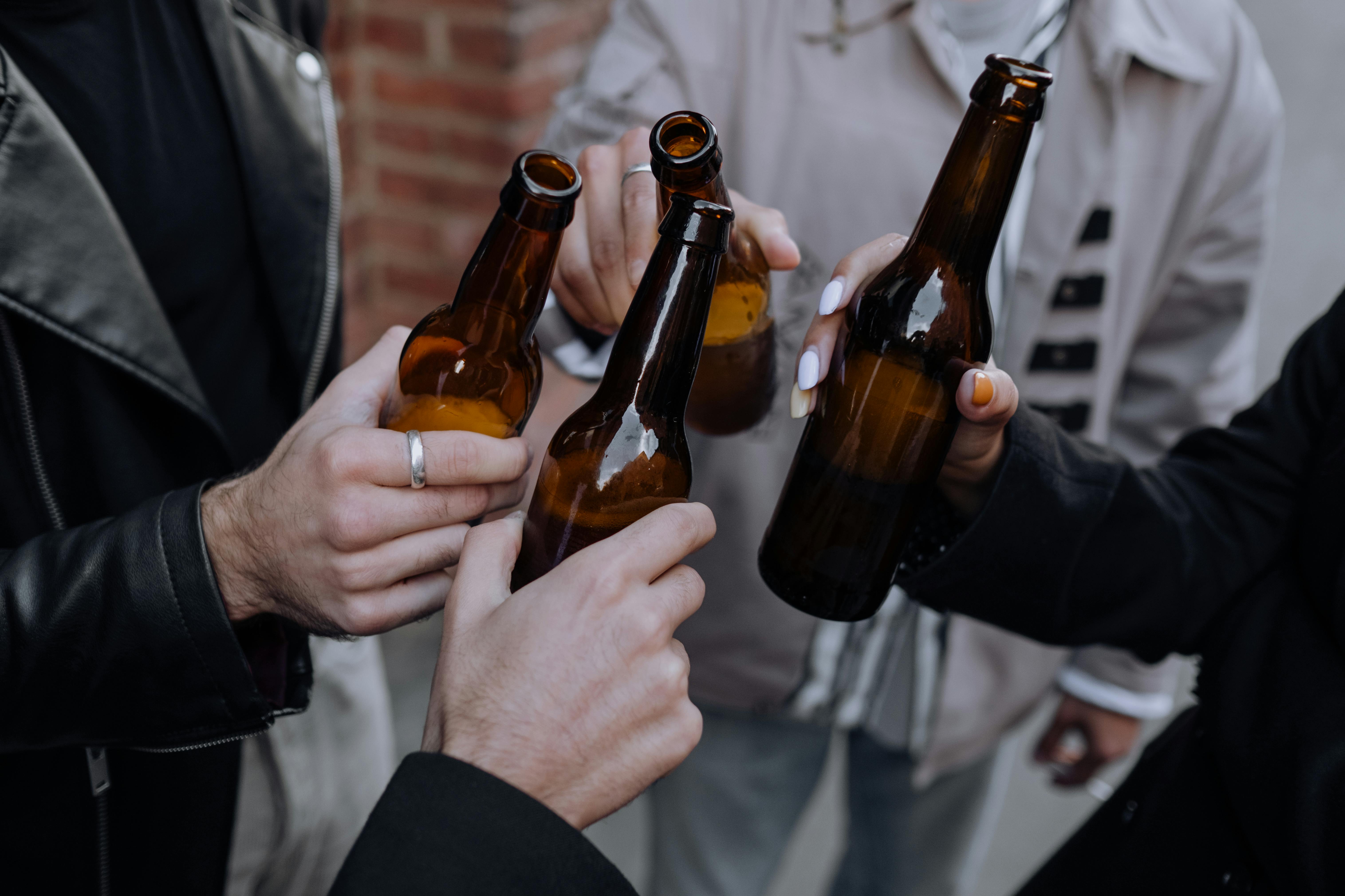 Hands of several people clinking brown beer bottles together in a casual social setting.