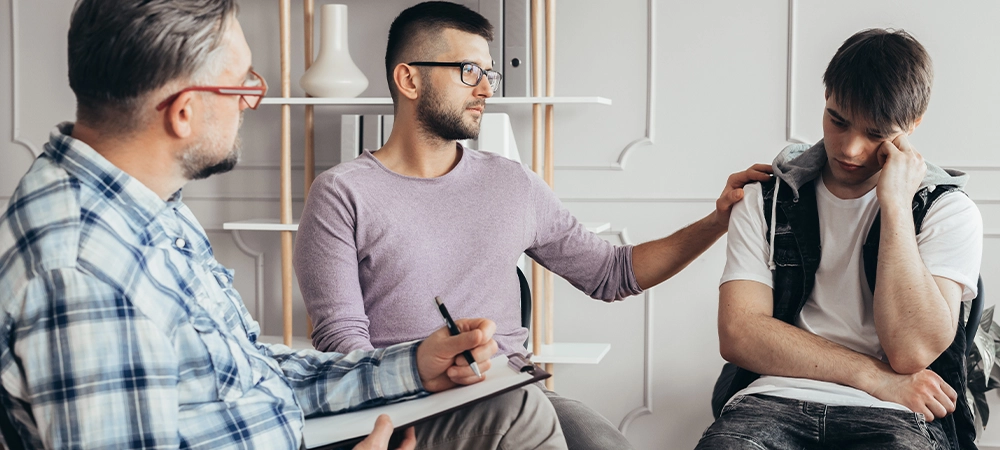 young man in glasses comforting his depressed friend during meeting with counselor